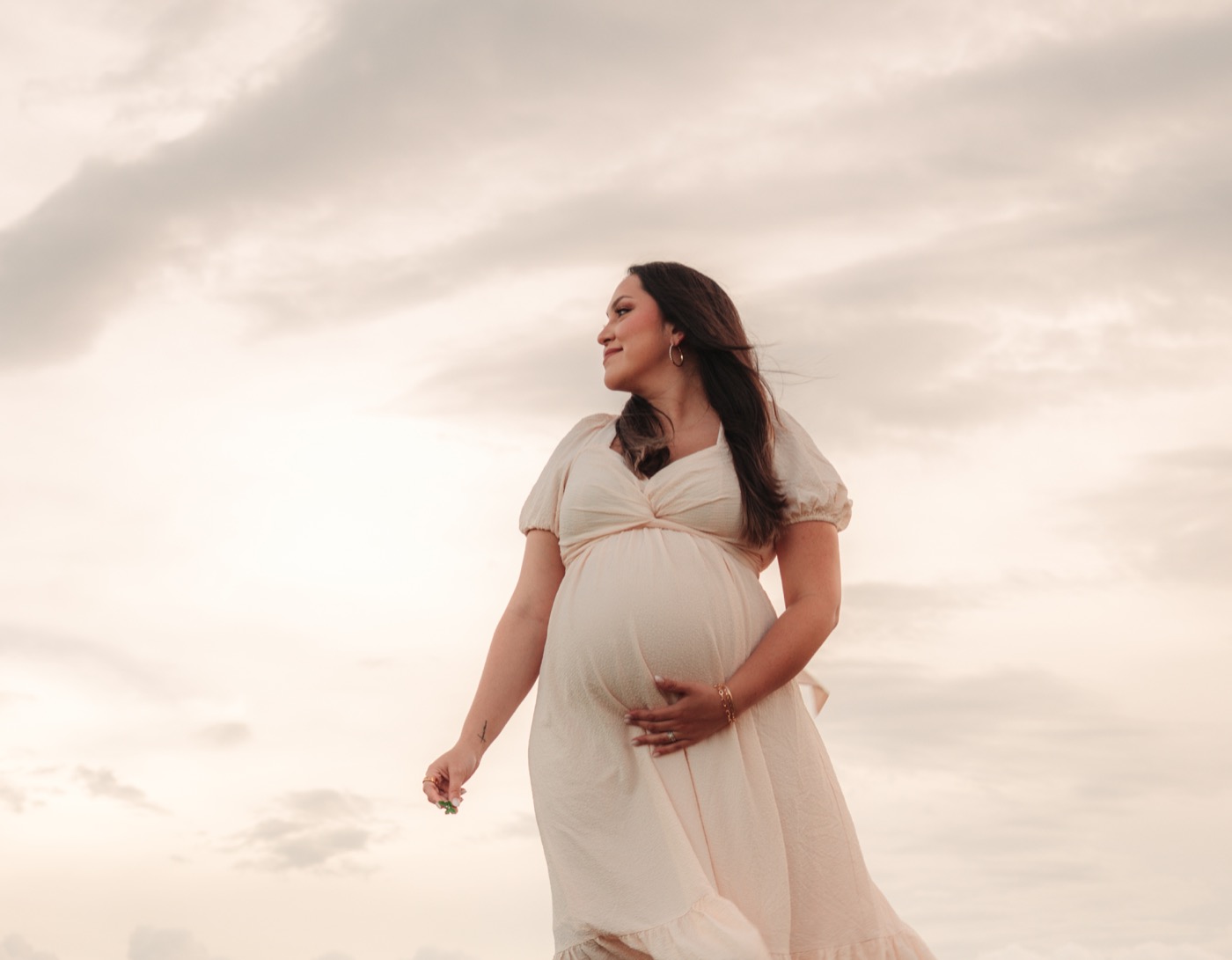 Retrato de maternidad con un vestido color crema bajo el cielo del atardecer